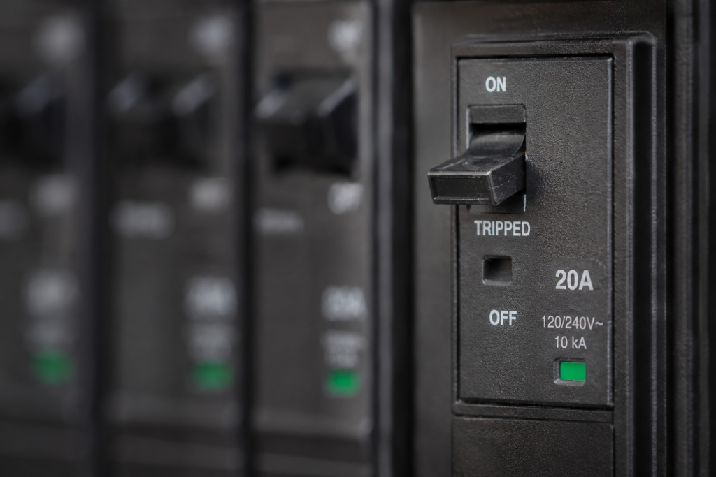 Macro close-up of a tripped circuit breaker in a residential electrical panel, showing the switch positioned between on and off with surrounding breakers blurred in the background.